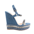 Christian Louboutin blue denim wedge sandals with silver pyramid studs on the straps, braided chevron-patterned wedge sole, and ankle buckle closure, shown in side profile on a white background.