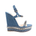 Christian Louboutin blue denim wedge sandals with silver pyramid studs on the straps, braided chevron-patterned wedge sole, and ankle buckle closure, shown in side profile on a white background.