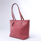 Angled front view of a pink Coach leather tote bag with long shoulder straps, gold-tone logo and matching leather hangtag on a white background.