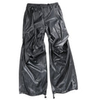 DIESEL oversized cargo trousers in black coated fabric with a glossy leather-look finish, elastic waistband, seam detailing, and adjustable drawstring hems, laid flat against a white background, Size 48 IT.