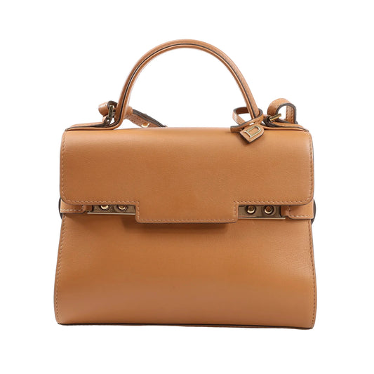 Delvaux Tempête PM handbag in smooth brown leather with top handle, adjustable shoulder strap, and gold-tone studded closure detail.