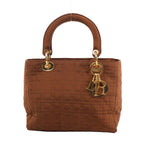 Front view of the Christian Dior Lady Dior Cannage Nylon Handbag in brown, showcasing quilted nylon with signature cannage stitching, dual rounded handles, gold-tone hardware, and dangling Dior letter charms, set against a white background.