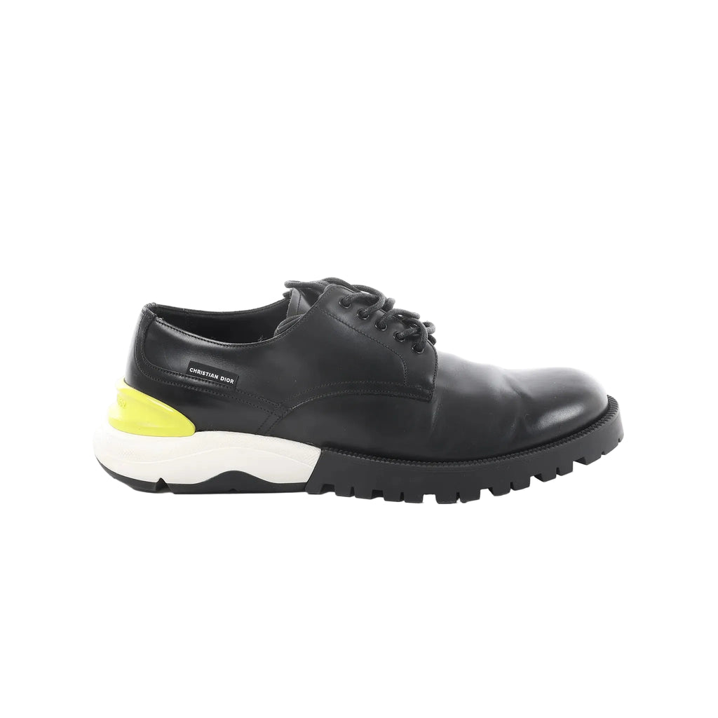 Black Dior leather derby shoe with lace-up front and chunky black lug sole with white midsole and neon yellow heel accent on white background