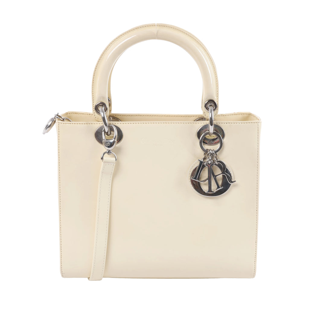 Dior Lady Dior beige leather handbag with rounded top handles, silver-tone letter charms and detachable shoulder strap on white background.