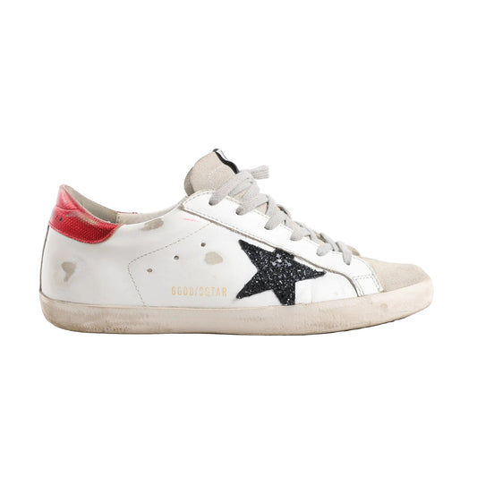 Golden Goose Super-Star Leather Sneakers in white with black glitter star patch, red heel tab, grey laces, and intentionally distressed detailing on the sole and upper, Size 40 EU, displayed in a side profile against a white background.
