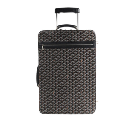 Goyard Trolle PM travel bag in brown featuring the signature Goyardine PVC canvas pattern, black leather trim, telescopic handle, and front zip pocket, shown upright on a white background.