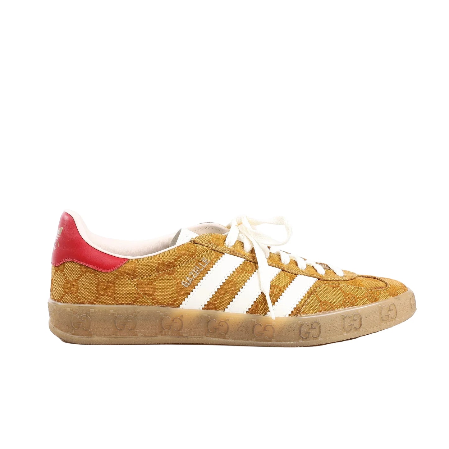 Gucci x Adidas Gazelle GG Canvas Sneakers in brown featuring GG monogram canvas upper, white leather three stripes, red heel tab with Adidas logo, cream laces, and translucent sole with embossed GG pattern, displayed on a white background.
