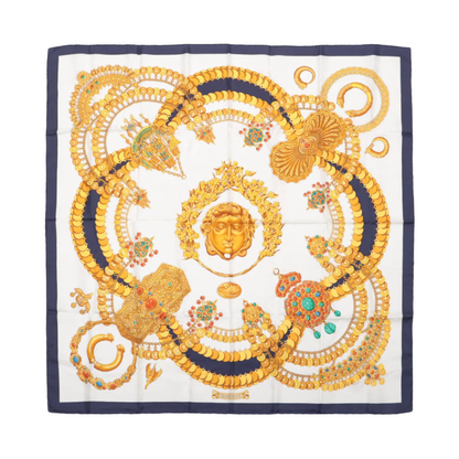 A Hermès silk scarf featuring a geometric pattern with gold and beige colors and decorative elements.