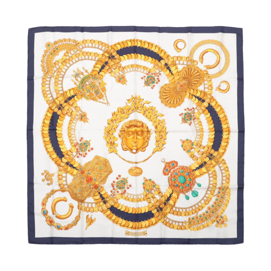 A Hermès silk scarf featuring a geometric pattern with gold and beige colors and decorative elements.