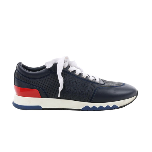 Side view of a navy blue Hermès Addict leather sneaker in size 43 EU, featuring white laces, perforated side panels, a red heel accent, and a white midsole with blue and black detailing on a white background.
