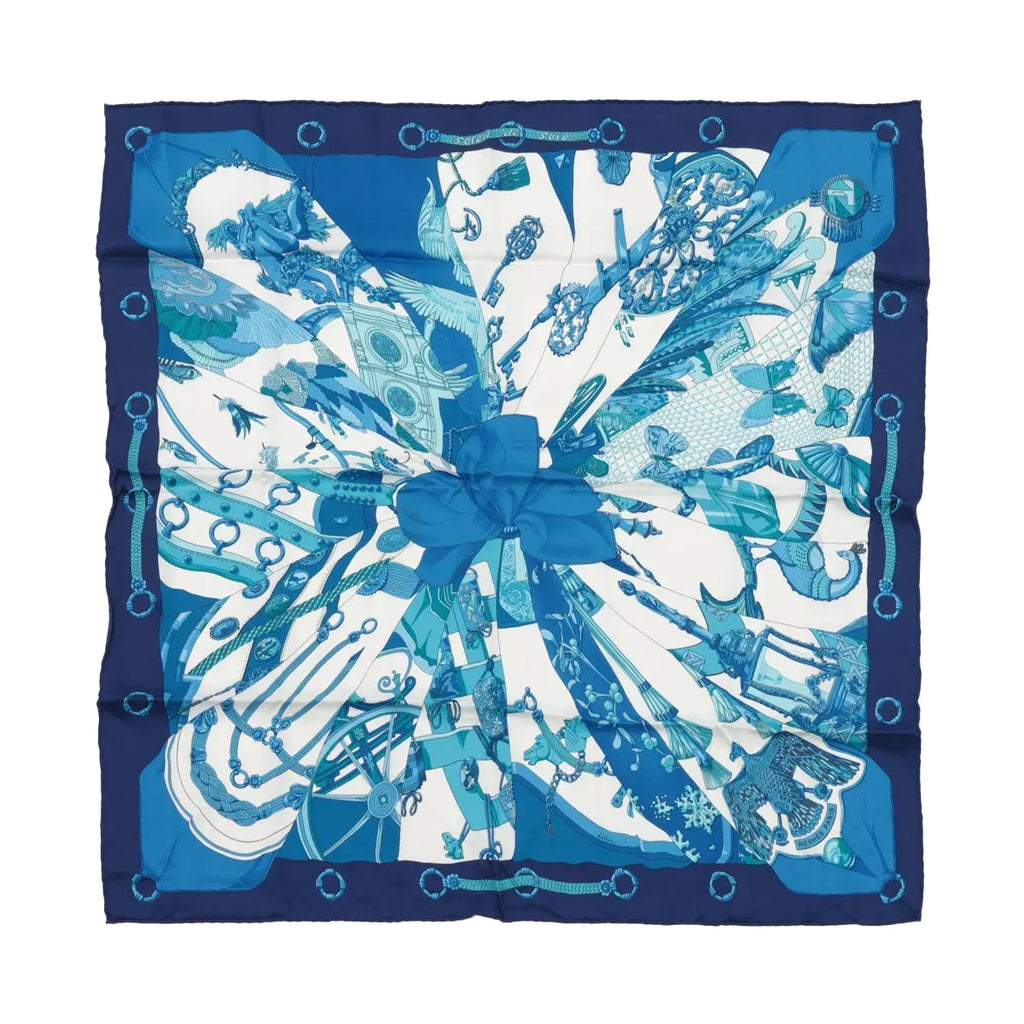 Hermès Carré 70 “Soleil de Soie” silk scarf in blue with navy border, blue sunburst-style panels, and central bow motif.
