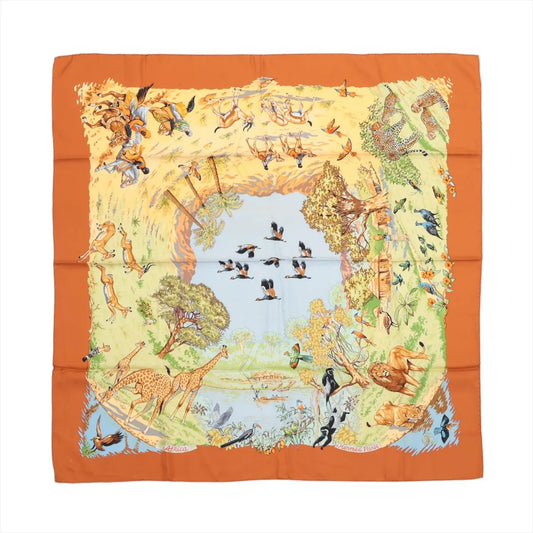 Hermès Carré 90 "Africa" silk scarf in brown featuring a central watering hole surrounded by a dynamic border of African wildlife, including giraffes, lions, birds, leopards, antelopes, and trees, all illustrated in earthy tones with an orange border.