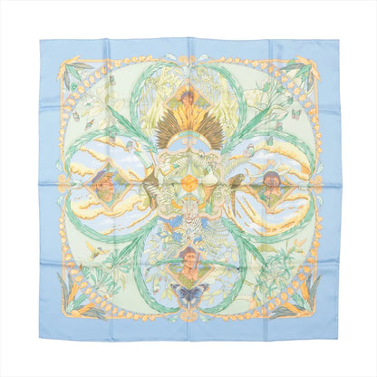 Hermès Carré 90 "Amazonia" silk handkerchief in blue, featuring intricate depictions of jungle foliage, birds, butterflies, a jaguar, and indigenous figures framed by golden botanical motifs, set against a soft sky-blue border for a rich tropical aesthetic.