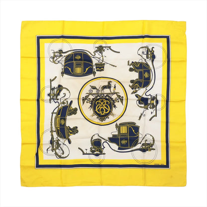 Hermès Carré 90 "Attelage en Arbalète" silk handkerchief in yellow, showcasing a symmetrical navy and gold carriage motif with a central medallion and bold yellow border.