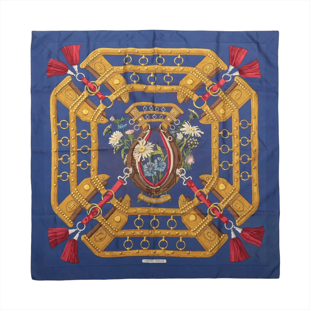 Hermès Carré 90 navy blue silk scarf with golden horse harness motifs, red tassels and a floral horseshoe design at the centre.