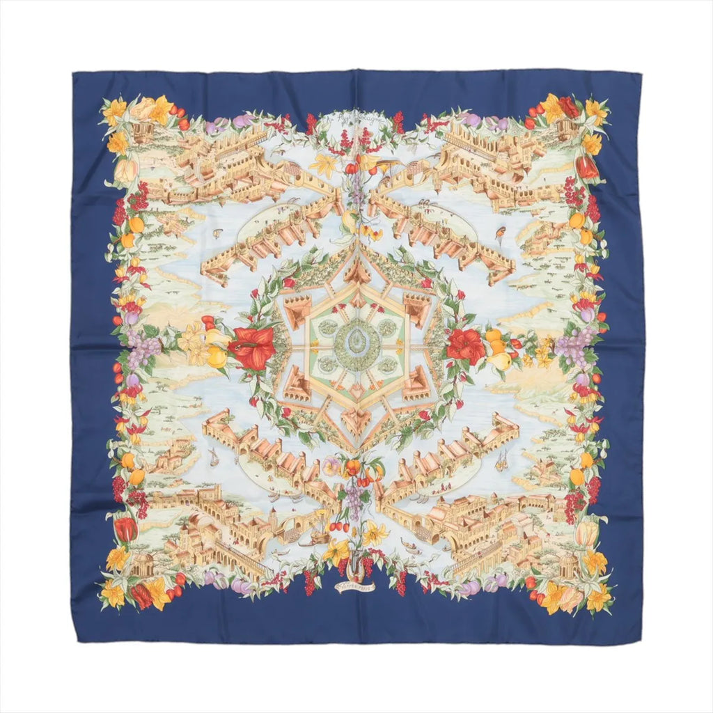 Hermès Carré 90 “Au Pays de Cocagne” silk scarf with navy border, central architectural landscape design, and multicolor floral and fruit border.