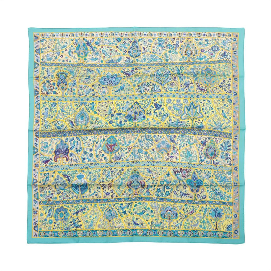 Flat view of a square Hermès Carré 90 silk scarf with a turquoise border and yellow field filled with blue floral, bird and botanical motifs.