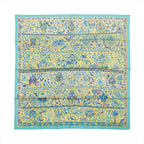 Flat view of a square Hermès Carré 90 silk scarf with a turquoise border and yellow field filled with blue floral, bird and botanical motifs.