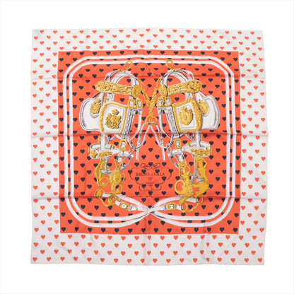 Hermès Carré 90 "Brides de Gala Love" silk scarf in red and white with gold bridles, navy and red heart pattern on border, and matching heart-shaped orange Hermès box.