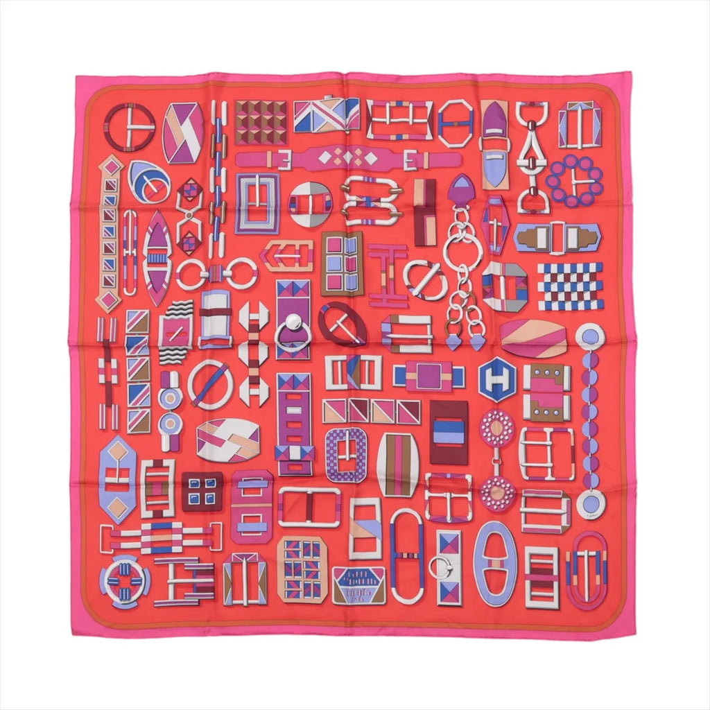 Hermès Carré 90 red silk scarf with allover geometric buckle and strap illustrations in pink, purple, blue, and white, framed by a pink border.