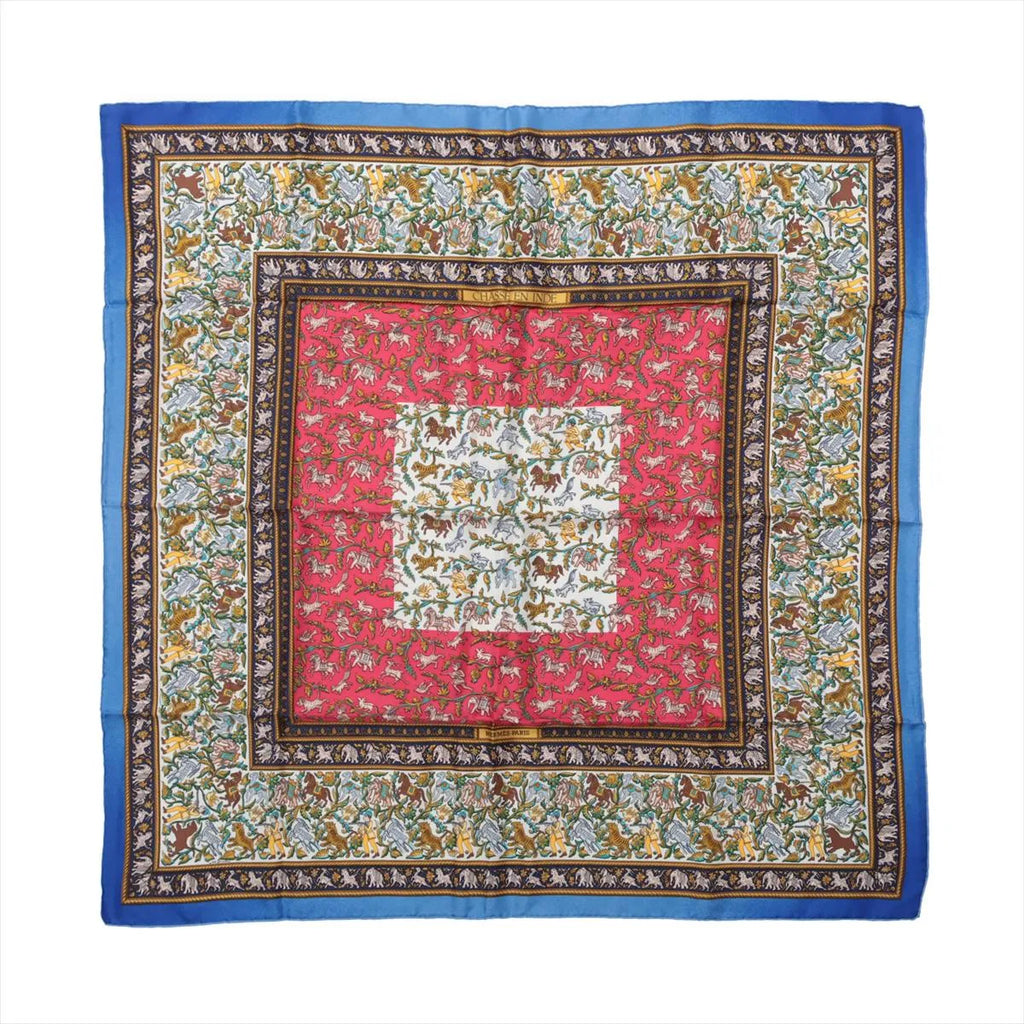 Blue Hermès Carré 90 silk scarf with red and ivory panels, intricate hunting scenes, animal motifs and ornate patterned borders.
