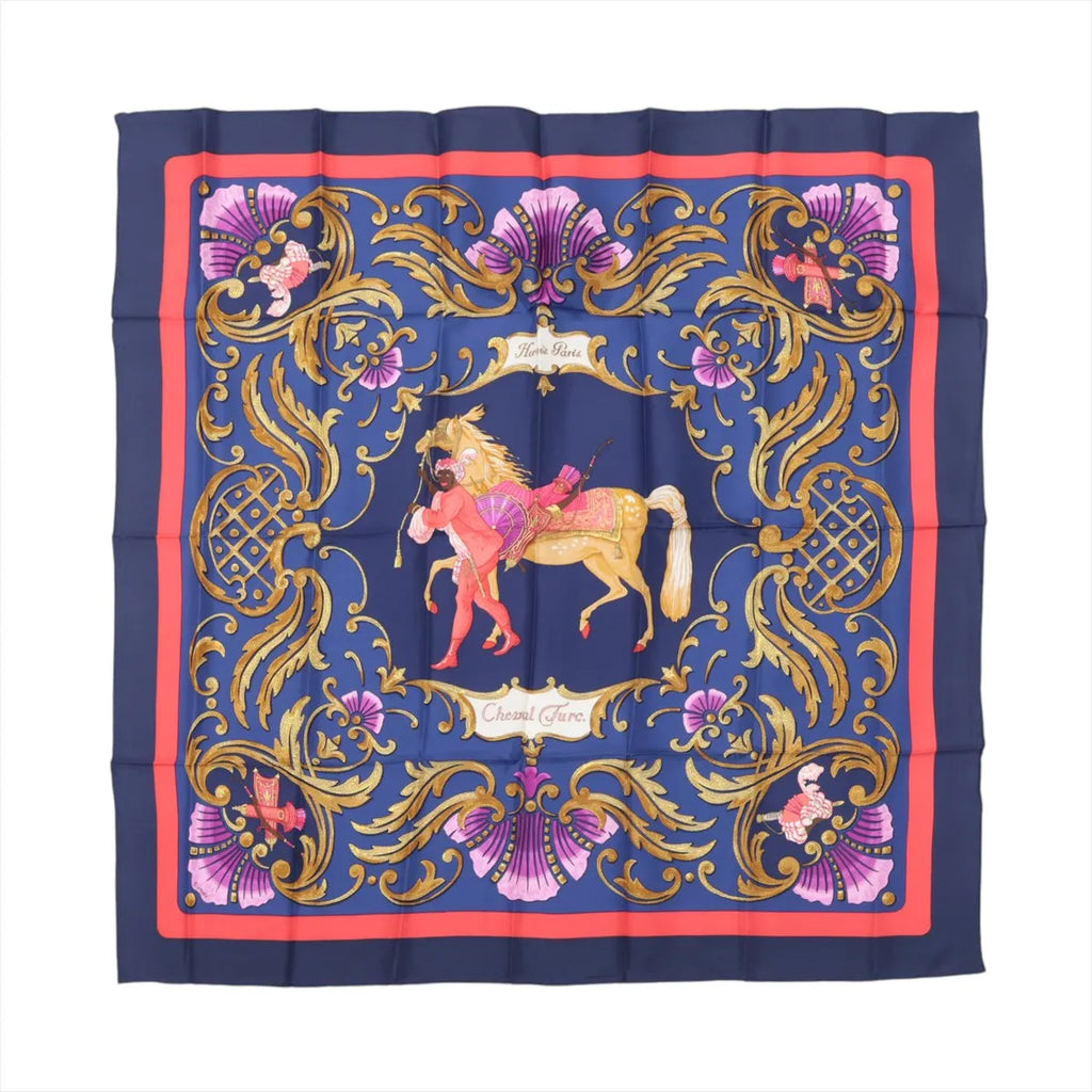 Hermès Carré 90 navy silk scarf with ornate gold baroque scrollwork, pink decorative accents, and central horse and figure illustration, framed by a red border.