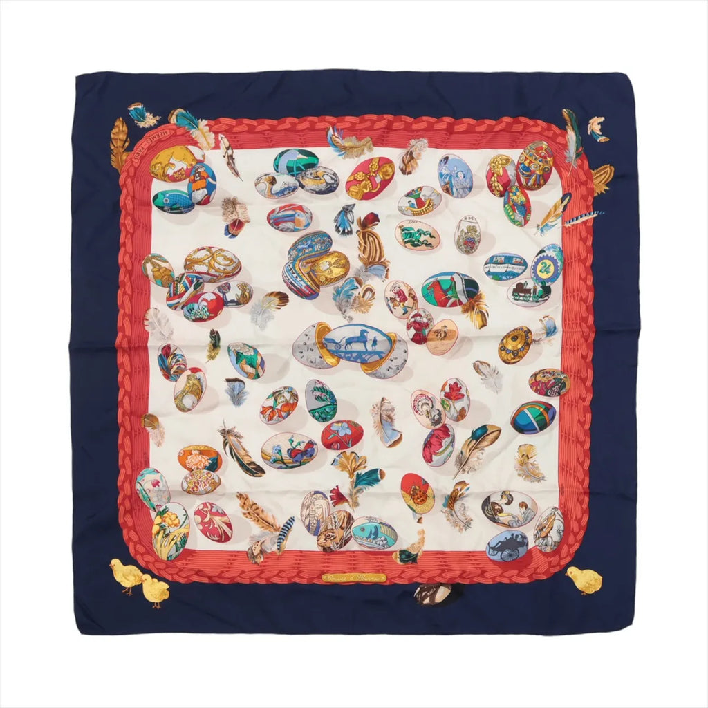 Hermès Carré 90 navy silk scarf with red braided border and cream center featuring multicolor illustrated eggs and scattered feather motifs.