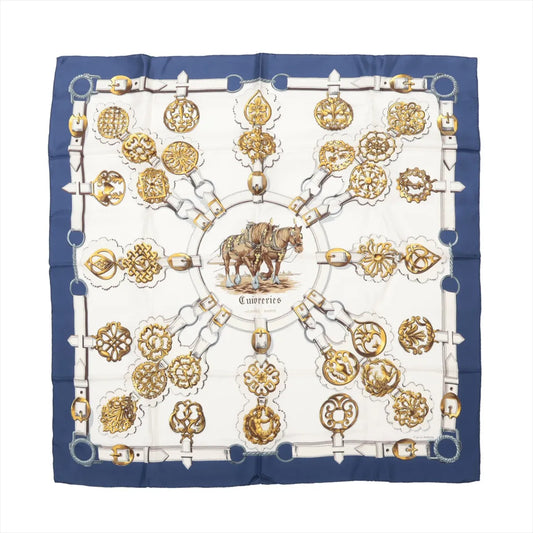 Hermès Carré 90 "Cuivreries" silk scarf in navy blue and white, featuring a central image of two horses surrounded by ornate golden bridle hardware in a circular layout, bordered with belt and buckle motifs.