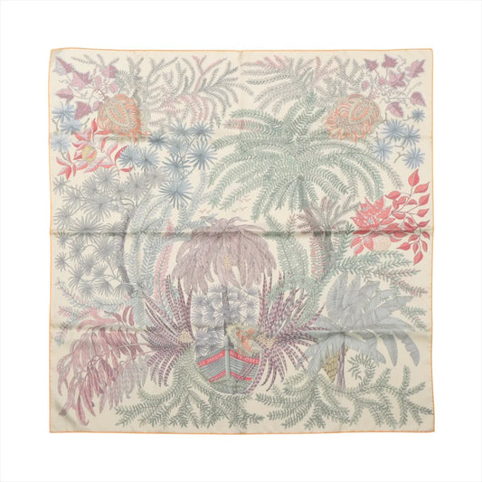 Flat-lay of a Hermès Carré Double Face 90 "Les Jardins des Peintres" silk scarf featuring a soft multicolor botanical illustration with palm leaves, flowers, and foliage in pastel tones on a cream background.