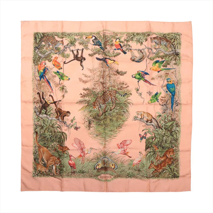 Hermès Carré 90 "Équateur" silk handkerchief in pink, featuring a detailed tropical jungle design with leopards, monkeys, parrots, toucans, flamingos, and lush greenery, bordered by a soft pink frame and centered around a large tree.
