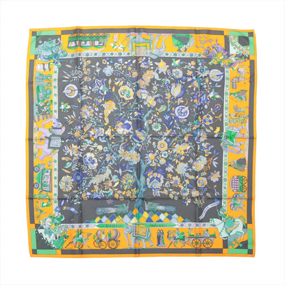 Flat-lay of a Hermès Carré 90 "Fantaisies Indiennes" silk scarf in navy blue and yellow, featuring elaborate floral patterns at the center with a vibrant border of Indian-inspired motifs, elephants, and decorative elements in multicolored detail.