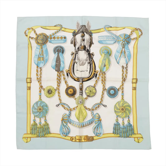 Hermès Carré 90 silk scarf in light blue featuring a central horse head surrounded by bridles, rosettes, and cockades in gold, blue, and green accents.