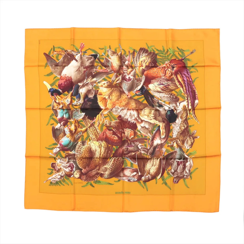 Hermès Carré 90 orange silk scarf with multicolor wildlife collage motif and green foliage accents, laid flat