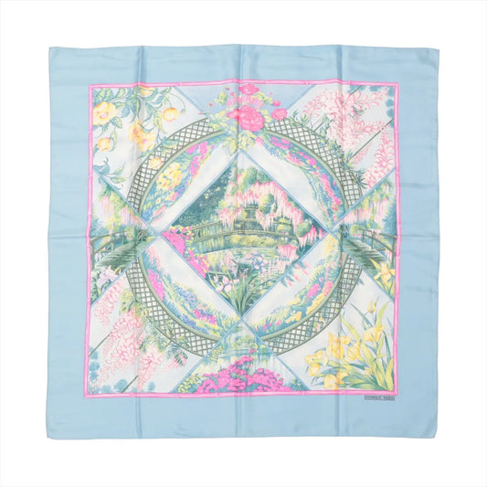 Hermès Carré 90 "GIVERNY" silk handkerchief in light blue, showcasing a central garden and bridge scene surrounded by floral panels with yellow irises, wisteria, roses, and trellises, bordered in pink and printed on luxurious silk twill.