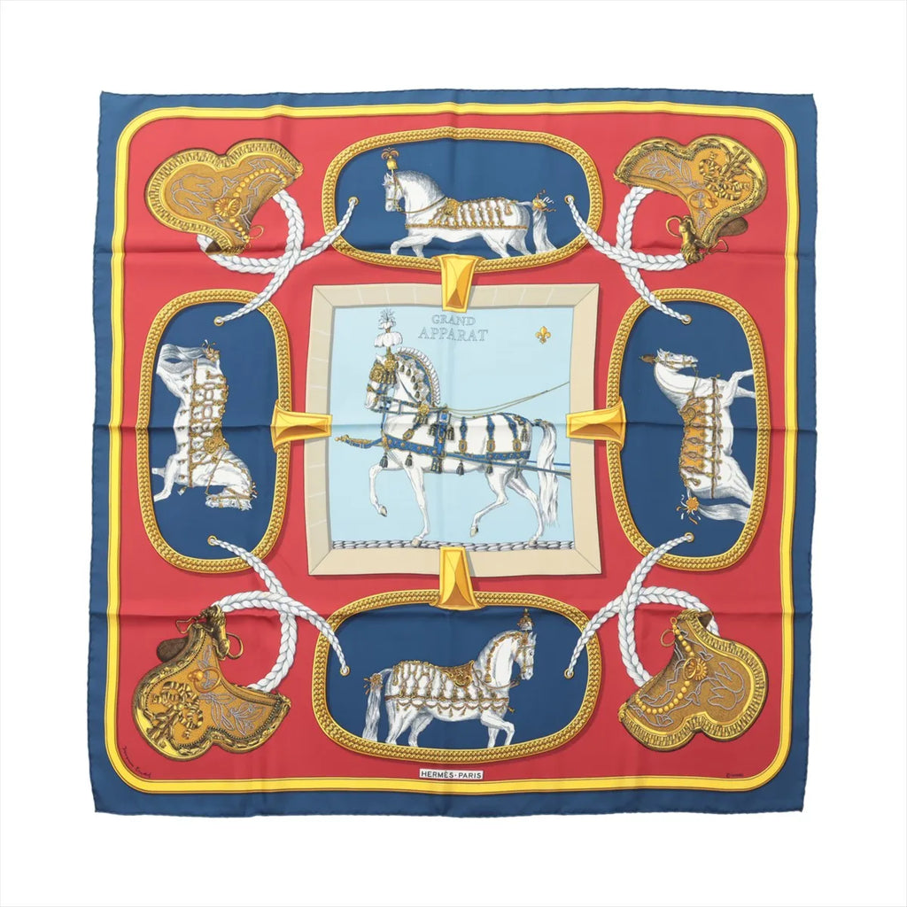 Hermès Carré 90 navy and red silk scarf with “Grand Apparat” horse and harness illustration, gold saddle motifs, braided rope details, and central framed horse design.