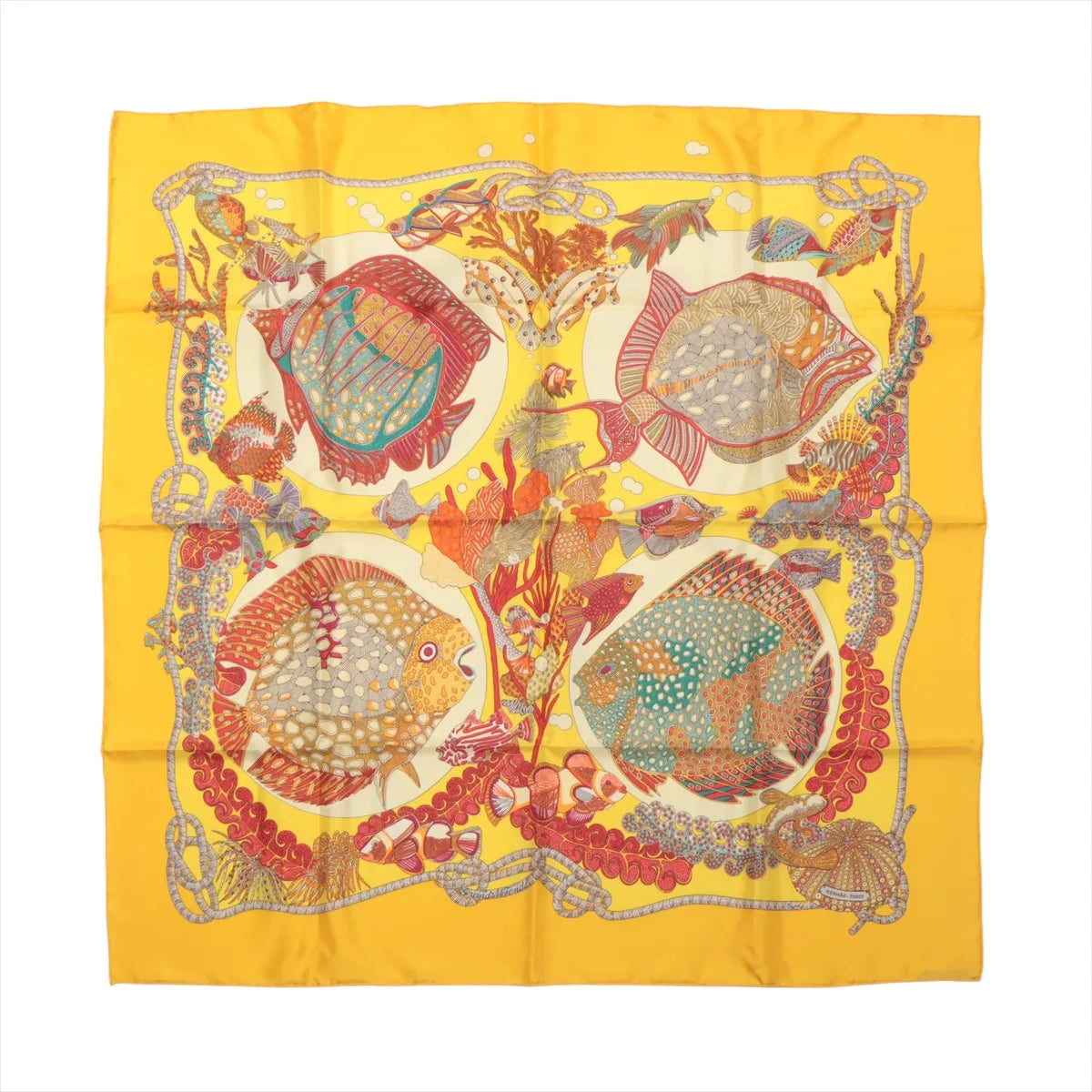 Flat-lay of a Hermès Carré 90 "Grands Fonds" silk scarf in yellow, showcasing an intricate underwater scene with multicolored tropical fish, coral reefs, and sea life framed by a vibrant yellow border.