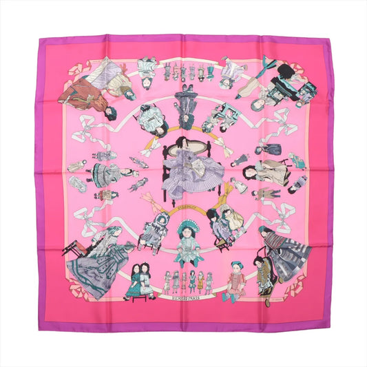 Hermès Carré 90 "HELLO DOLLY" silk scarf in pink featuring detailed illustrations of antique dolls, toys, and ribbon accents with a bold fuchsia border and central seated doll design, laid flat against a white background.