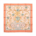 Hermès Carré 90 silk scarf in orange with pink center, gold scrollwork and floral motif, and orange border, laid flat