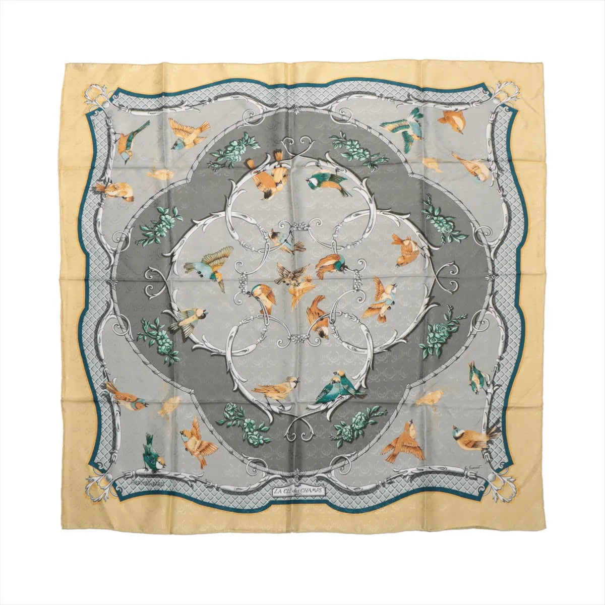 Hermès Carré 90 "La Clé des Champs" silk handkerchief in beige, showcasing colorful birds in flight and perched positions, arranged around a gray and silver ornamental frame with green foliage details and a scalloped border design.