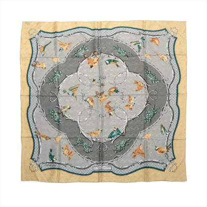 Hermès Carré 90 "La Clé des Champs" silk handkerchief in beige, showcasing colorful birds in flight and perched positions, arranged around a gray and silver ornamental frame with green foliage details and a scalloped border design.