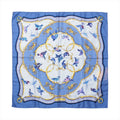 Hermès Carré 90 "La Clé des Champs" silk scarf in shades of blue featuring colorful birds in flight, ornate golden scrollwork, and a soft floral background framed by an elegant patterned border.