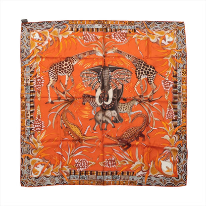 Hermès Carré 90 "La Marche du Zambèze" silk scarf in vivid orange featuring a central elephant surrounded by giraffes, crocodiles, and tropical plants, with intricate borders and rich patterns in brown, yellow, and ivory tones.