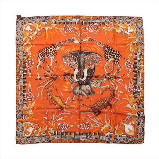 Hermès Carré 90 "La Marche du Zambèze" silk scarf in vivid orange featuring a central elephant surrounded by giraffes, crocodiles, and tropical plants, with intricate borders and rich patterns in brown, yellow, and ivory tones.