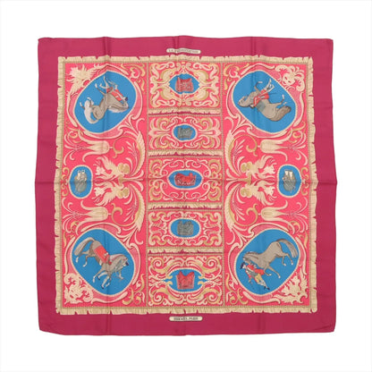 Hermès Carré 90 silk scarf in burgundy with a symmetrical layout of ornate gold scrolls, blue and red equestrian vignettes, and horses with riders on a rich silk twill.