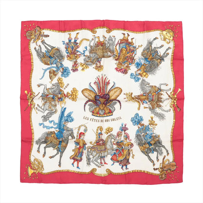 Hermès Carré 90 silk scarf titled "Les Fêtes du Roi Soleil," featuring elaborately costumed figures on horseback in vibrant red, gold, and blue tones, set against a cream background with a rich red border and ornate decorative flourishes.