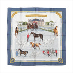 Hermès Carré 90 silk scarf in blue with an equestrian-themed design showing horses, riders, and a grand French estate in detailed illustrations.