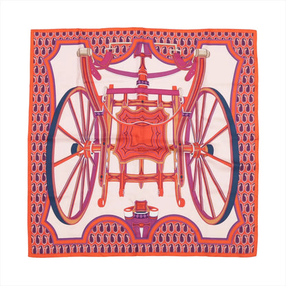 Hermès Carré 90 silk scarf in orange with a bold design of a decorative horse-drawn carriage and large wheels in pink, red, and purple on a light background.