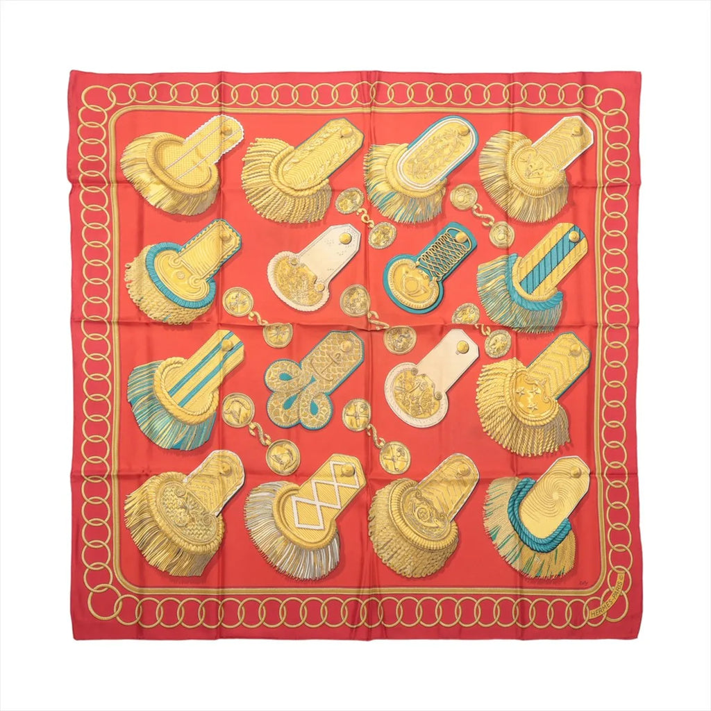 Flat view of a red Hermès Carré 90 silk scarf featuring gold military epaulettes, medallions, turquoise accents and a looping gold border.