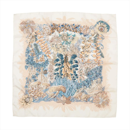 Hermès Carré 90 "L'Île Déserte" silk scarf featuring beige and blue botanical illustrations of flowers, leaves, and mushrooms on a cream background.