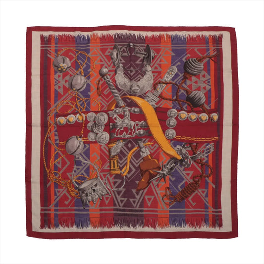 Hermès Carré 90 "Lujo Criollo" handkerchief in red with intricate illustrations of traditional Latin American ornaments, silver stirrups, spurs, ropes, and coins over a vibrant geometric background in red, orange, blue, and purple tones.